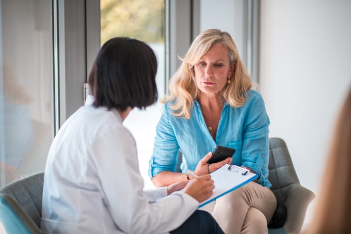 Photo shows a woman speaking with her doctor, who is writing on a clipboard/Getty Images