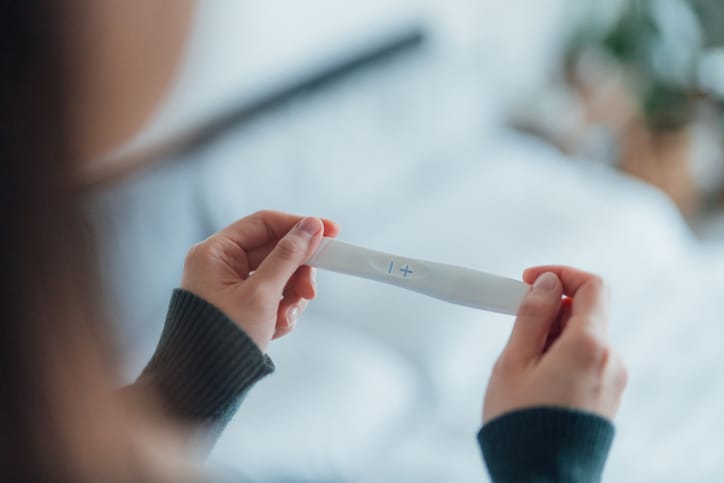 Photo shows a woman holding a pregnancy test kit and waiting for the result in her bedroom/Getty Images