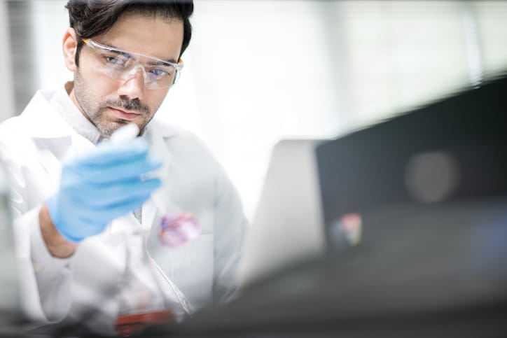 Photo shows a male scientist wearing eyeglasses experimenting and examining chemical sample a flask in a laboratory/Getty Images