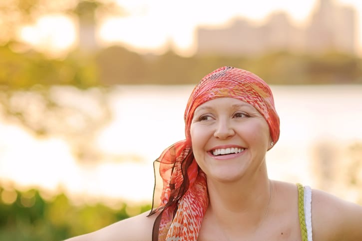 Photo shows a smiling woman with cancer wearing a scarf/Getty Images