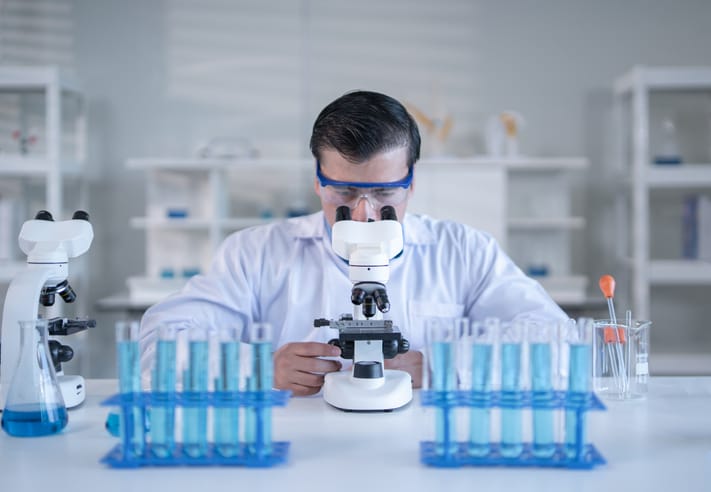 Photo shows a laboratory technician looking through a microscope/Getty Images
