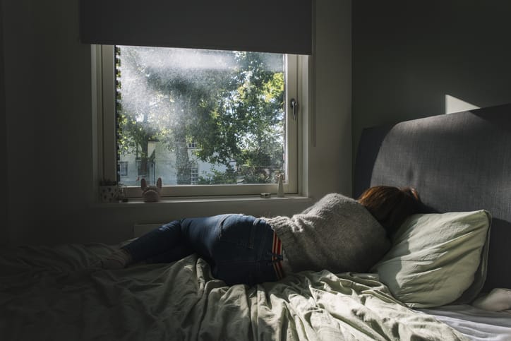 Photo shows a woman laying in bed facing a window/Getty Images