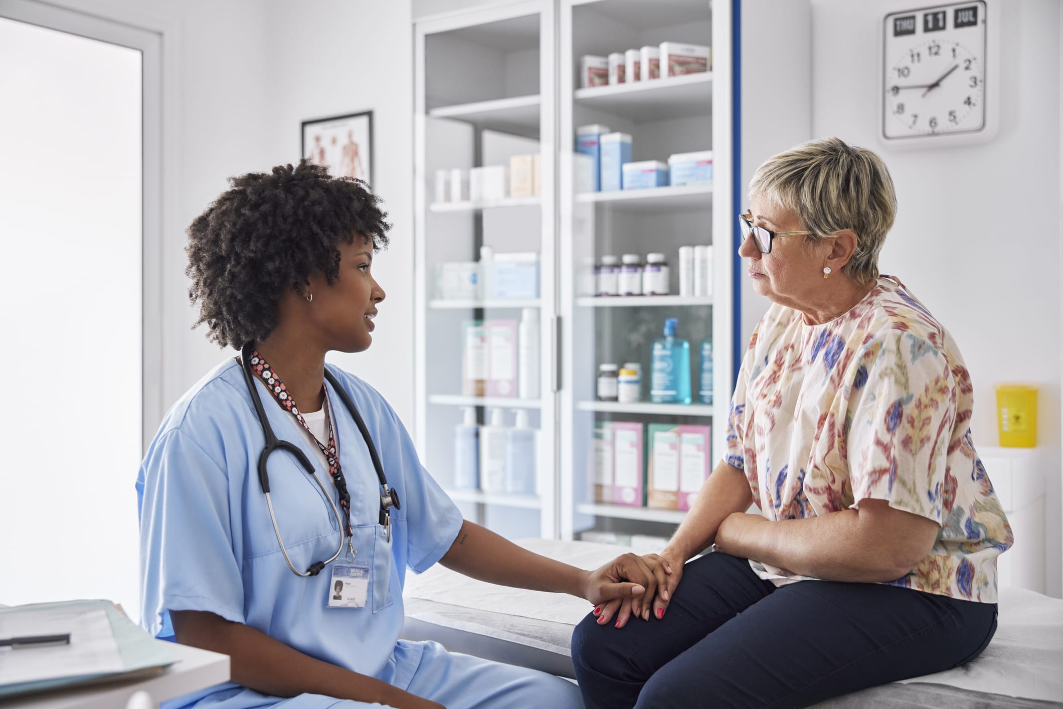 Female healthcare worker consoling patient sitting on examination table.