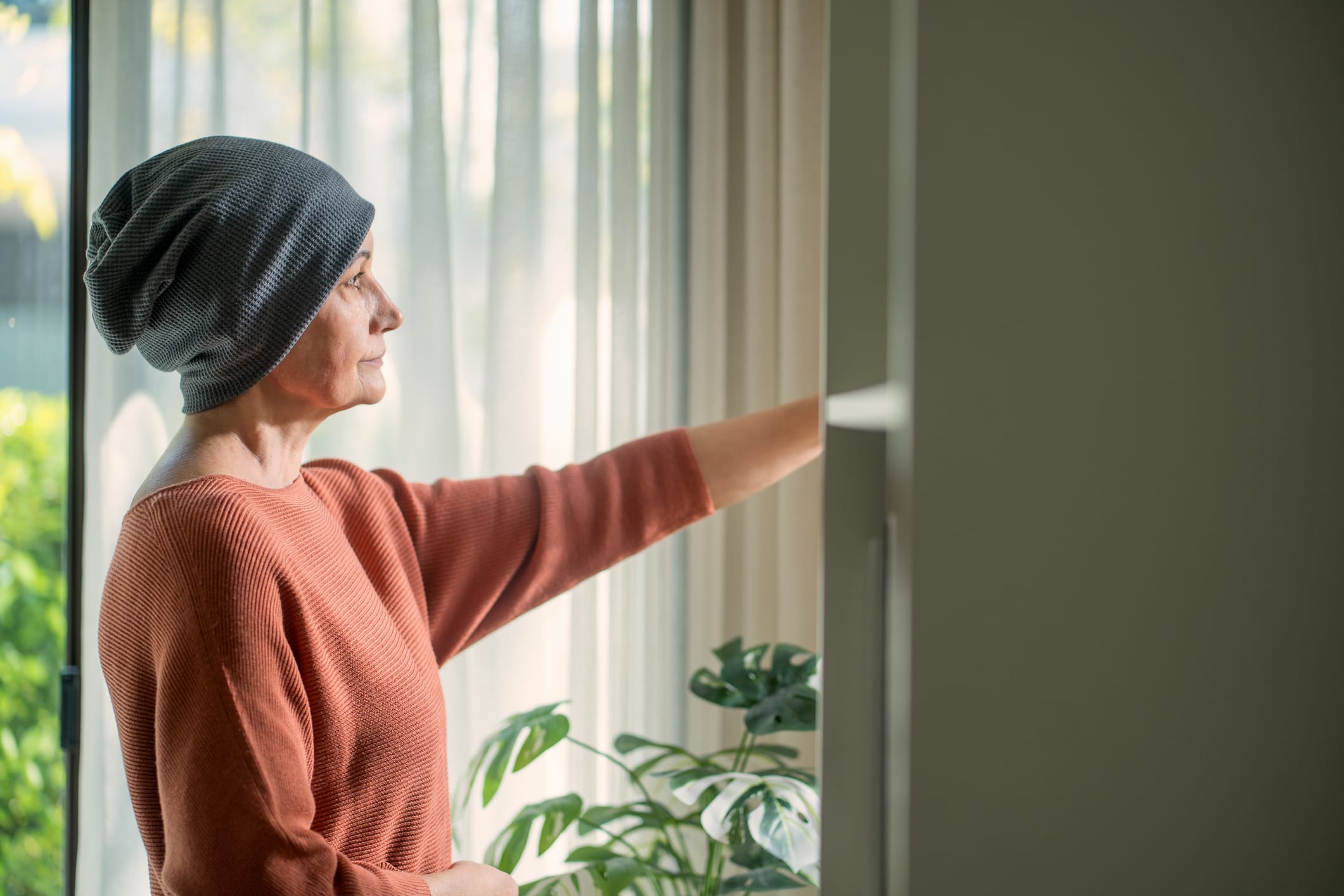 Senior woman with cancer stands by home window
