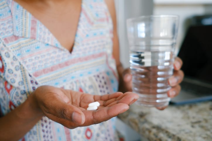 Photo shows a close-up of a woman in a kitchen taking medication/Getty Images