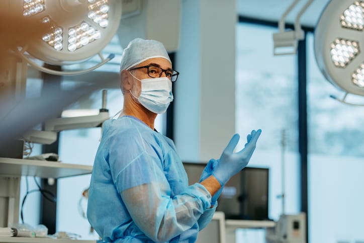 Photo shows a doctor putting on surgical gloves in an operating room/Getty Images