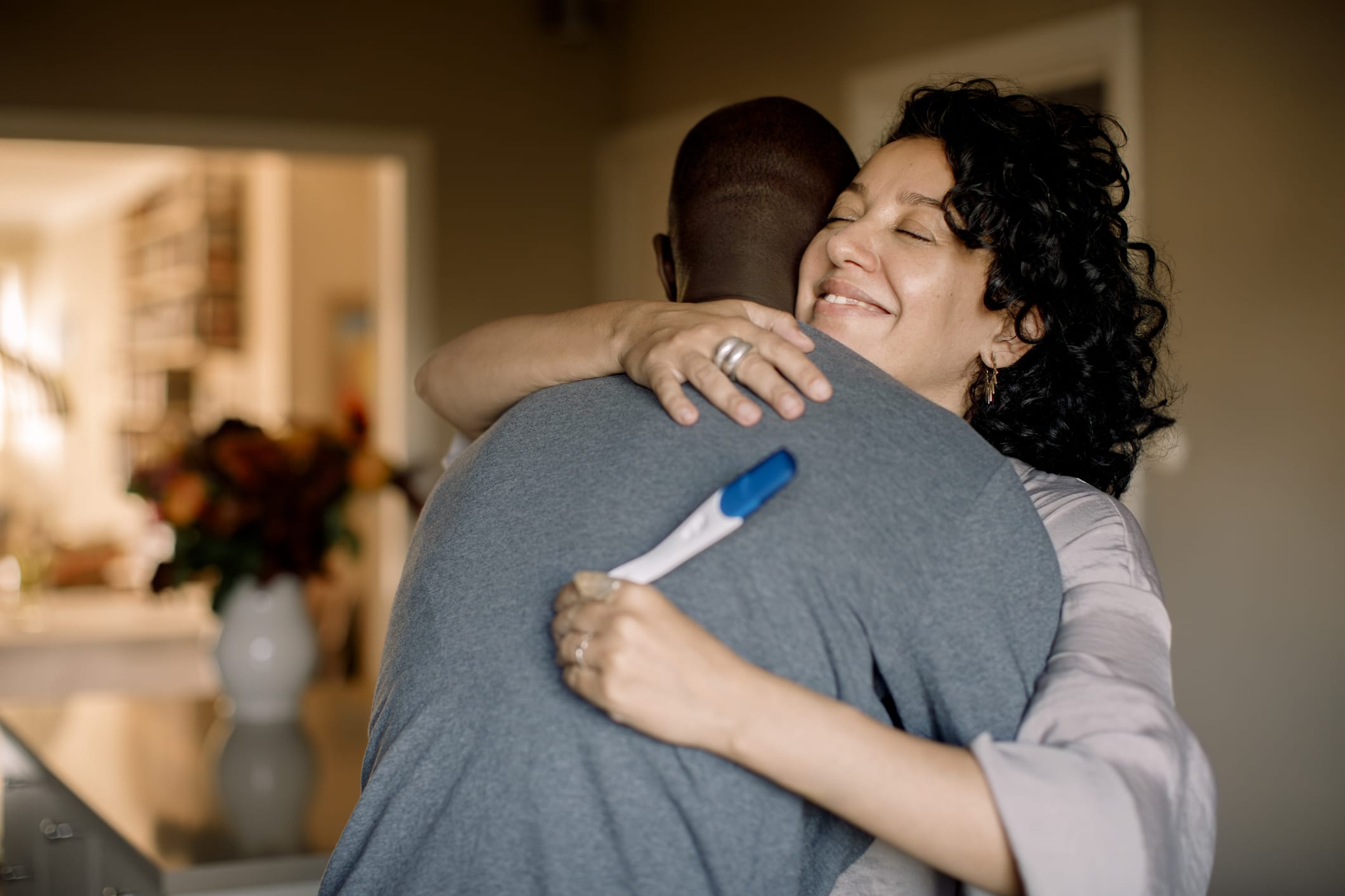 Smiling woman hugging man while holding a pregnancy test