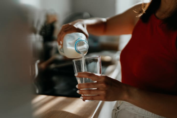 Photo shows a woman pouring a glass of milk in a kitchen/Getty Images