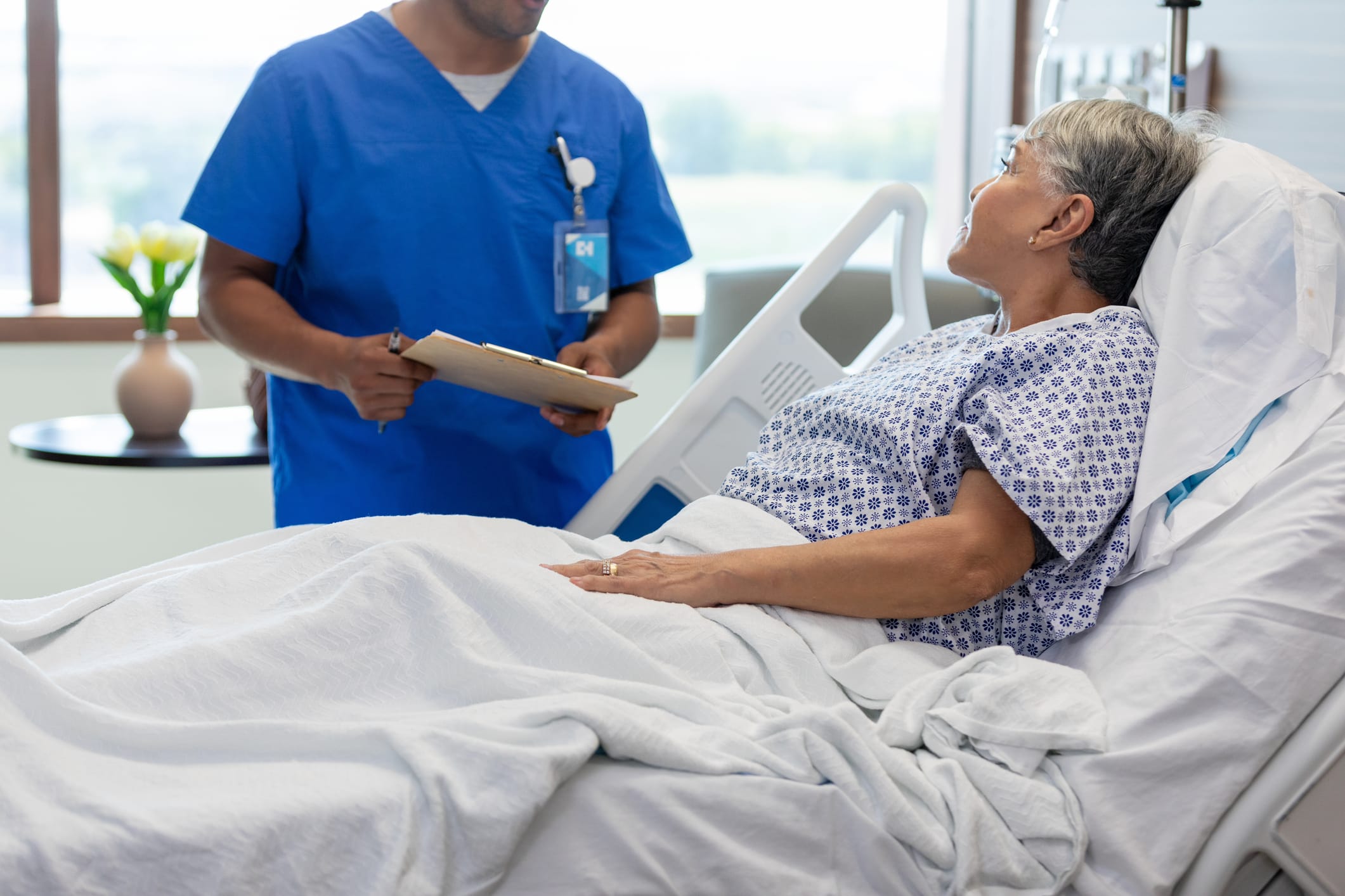 Female patient in hospital bed; doctor reviewing chart.