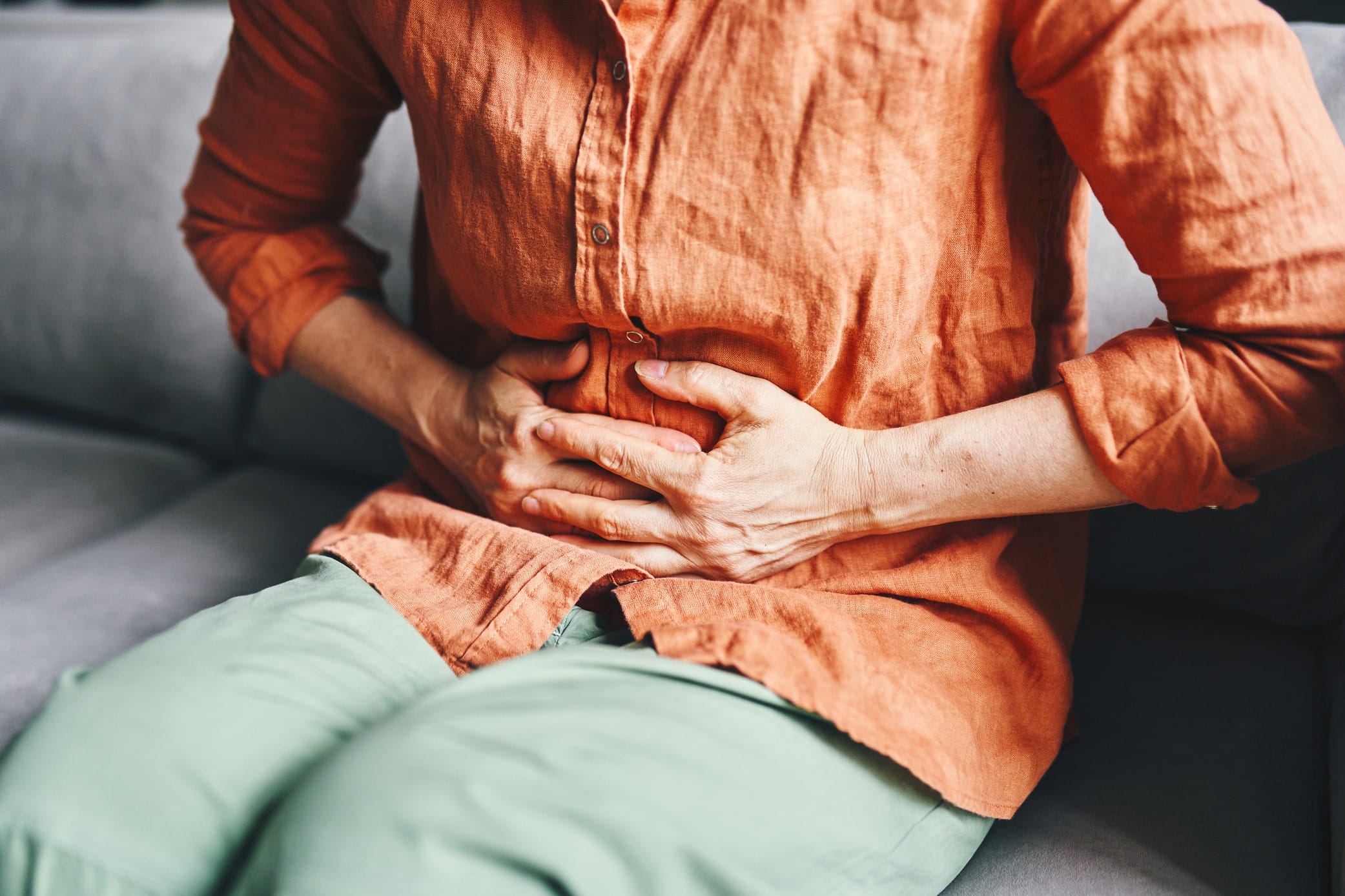 Woman sitting on couch clutching painful abdomen